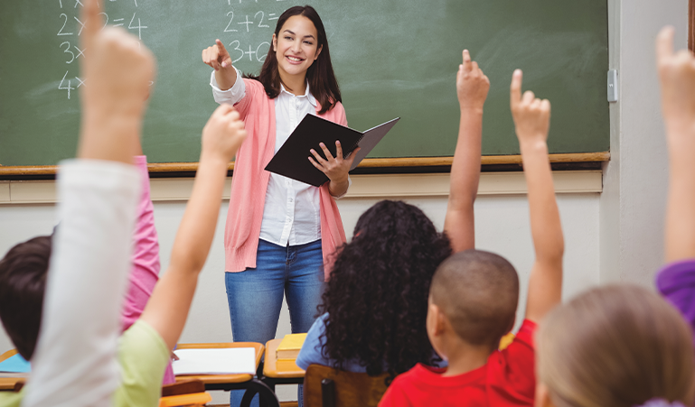 Teacher looking at group of students raising their hands.