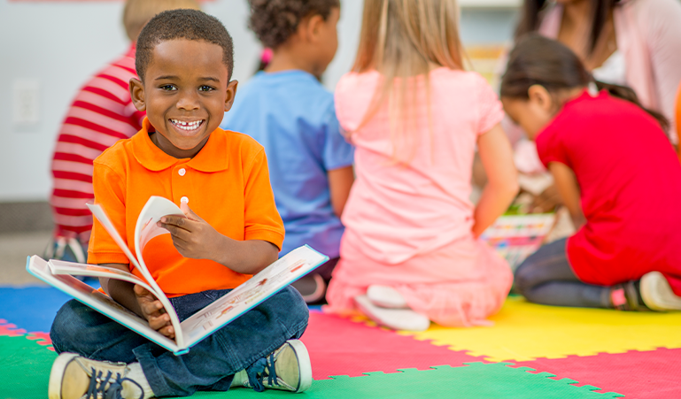 Child sitting down and reading a book with joy.