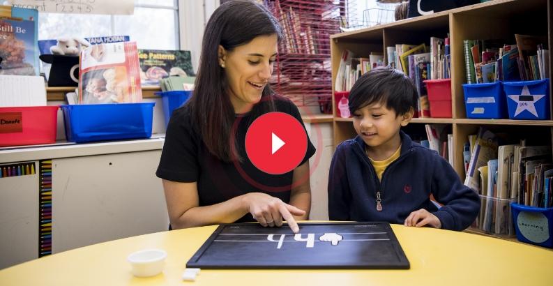 Teacher using magnetic lowercase letters on a blackboard to teach phonics to young students.