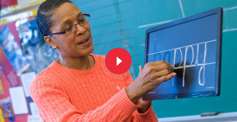 Teacher demonstrating the Wet-Dry-Try handwriting technique on a chalkboard with a student practicing letter formation.